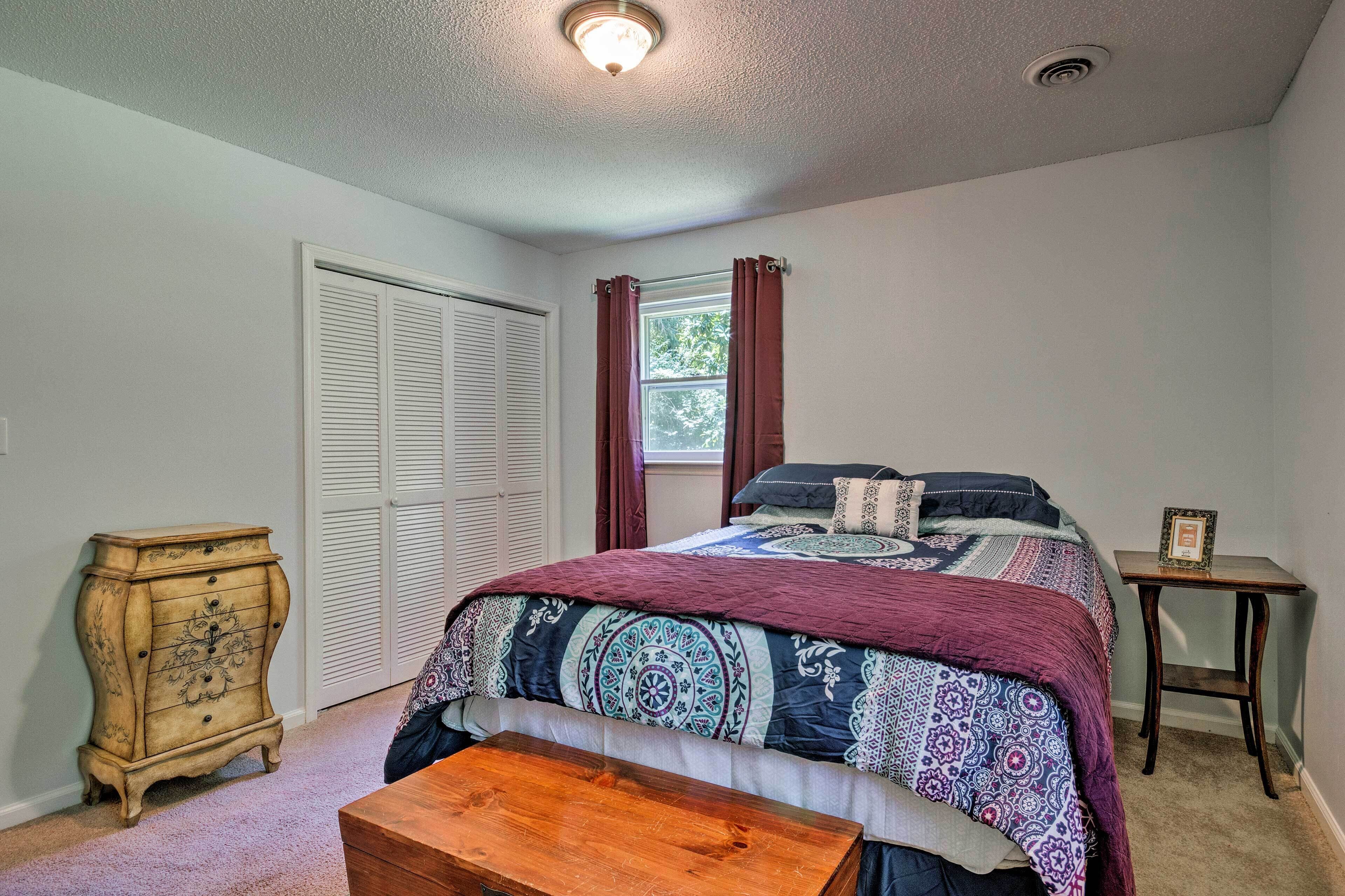 A bedroom with a bed, a dresser, a nightstand, and a window with curtains.