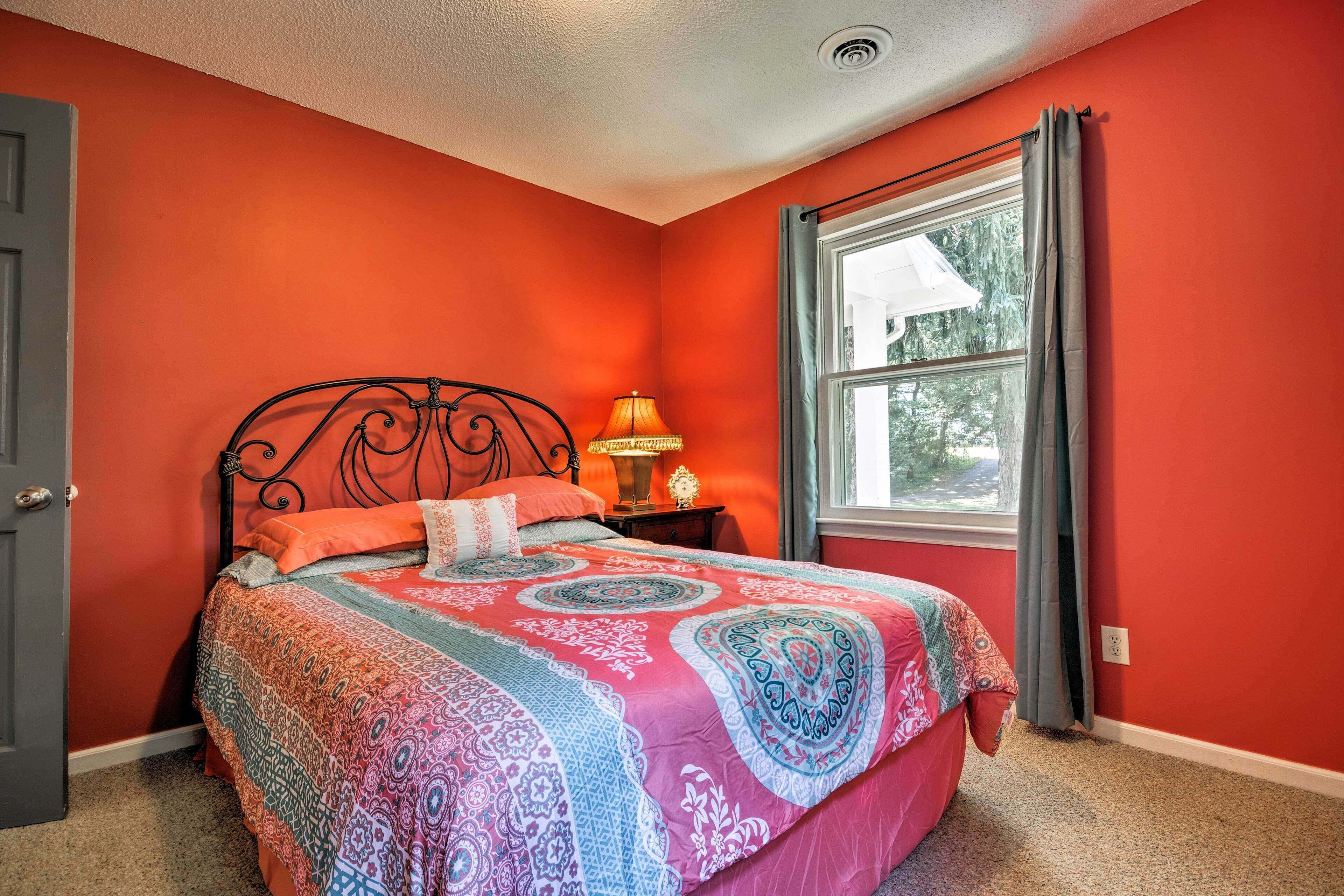 Un dormitorio con cama, mesita de noche, lámpara y ventana con cortinas.