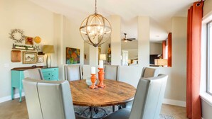 Un coin repas avec une table ronde en bois entourée de six chaises, un lustre et diverses décorations murales.