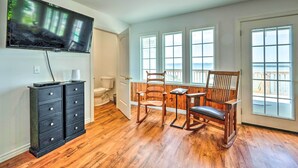 Ein Zimmer mit Holzboden, einem an der Wand befestigten Fernseher, einem Holzstuhl, einem kleinen Tisch und großen Fenstern mit Blick.