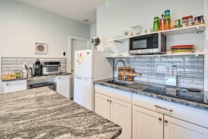 A modern kitchen with a granite countertop, white cabinetry, a built-in microwave, and a coffee maker. - Comfy Asheville Vacation Rental w/ Hot Tub! (Asheville)