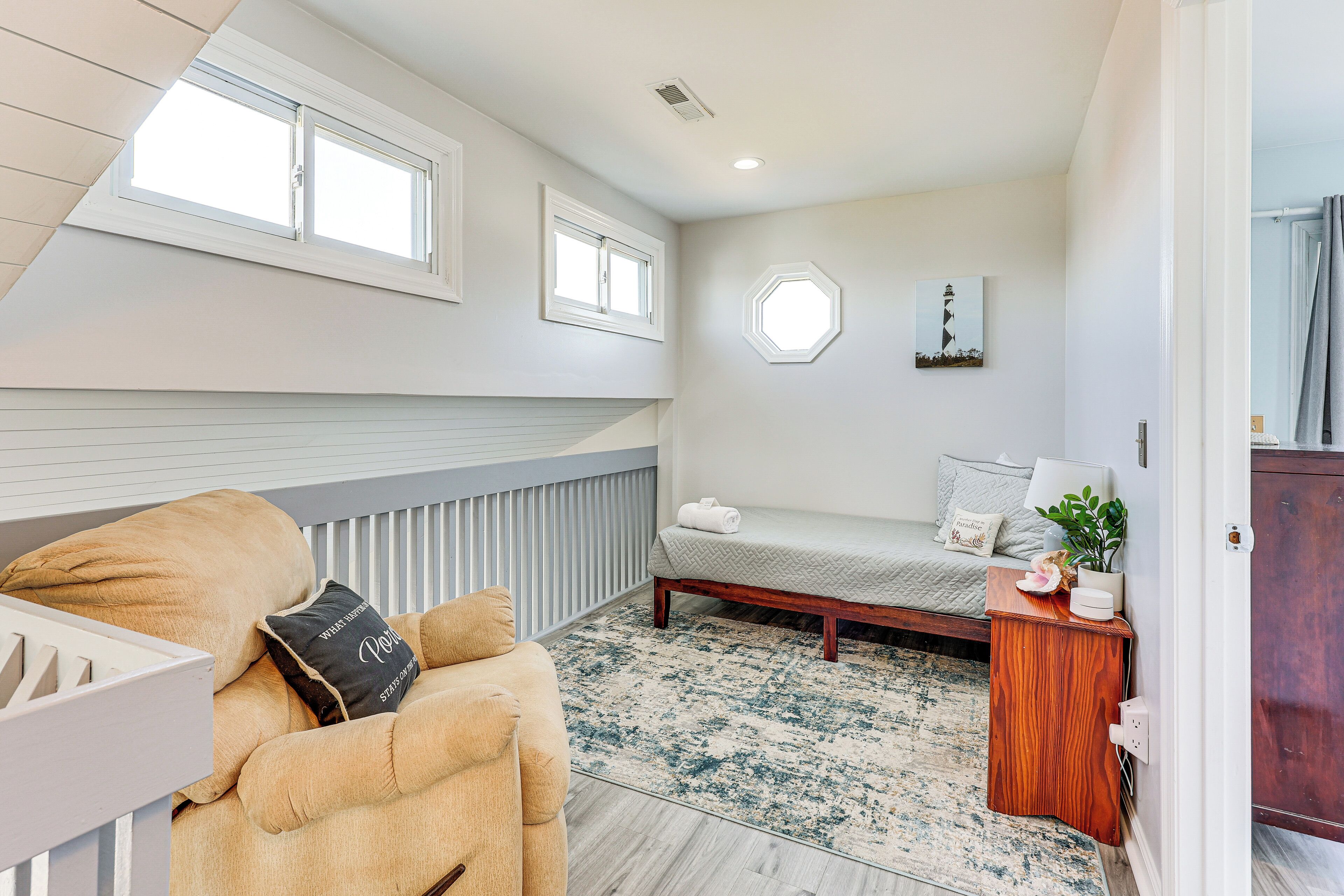 A bedroom with a bunk bed, a cushioned chair, a bedside table with a lamp, and a window with a view of the sky.