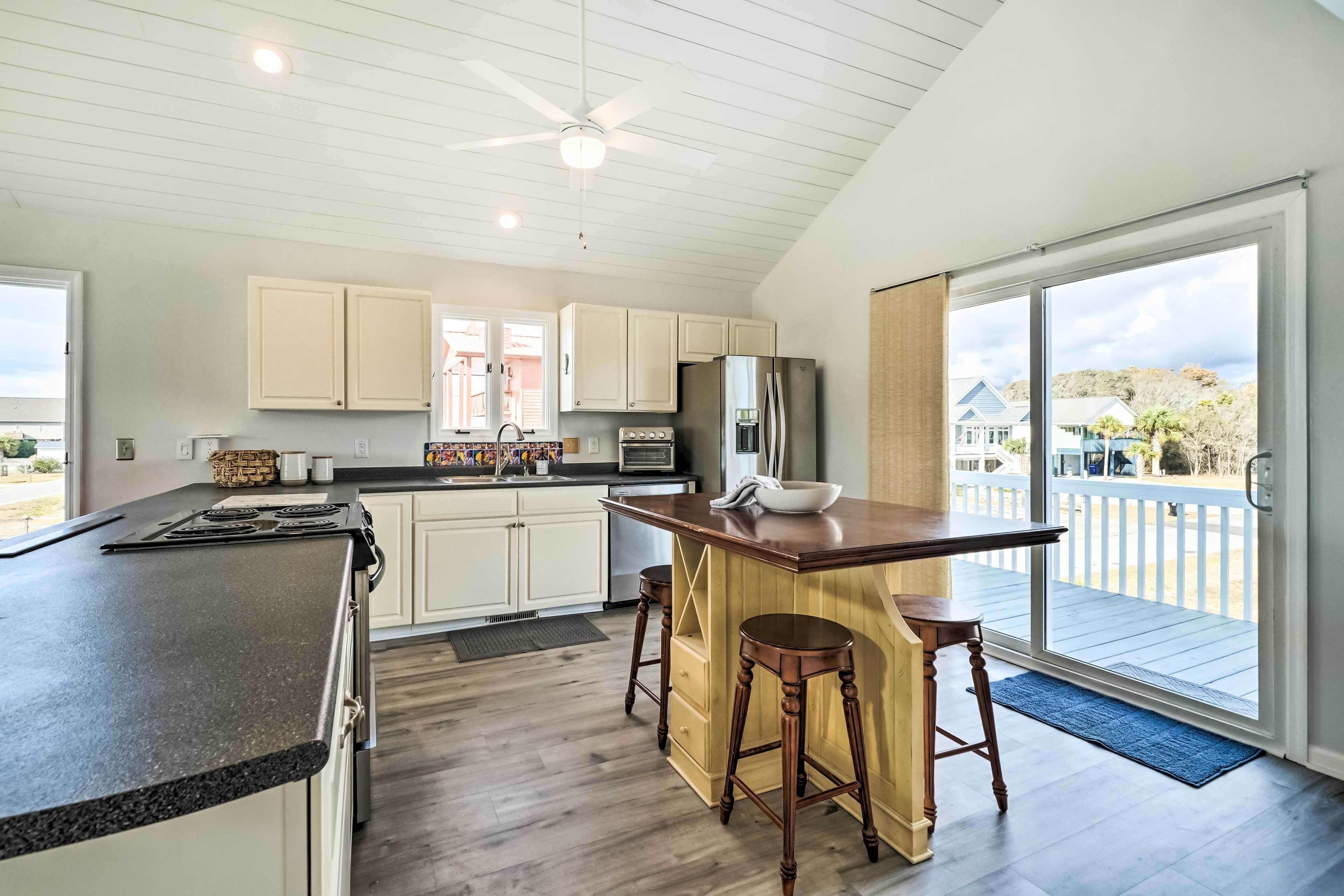 Una cocina moderna con armarios blancos, una isla central con taburetes, un refrigerador grande y vistas al exterior.