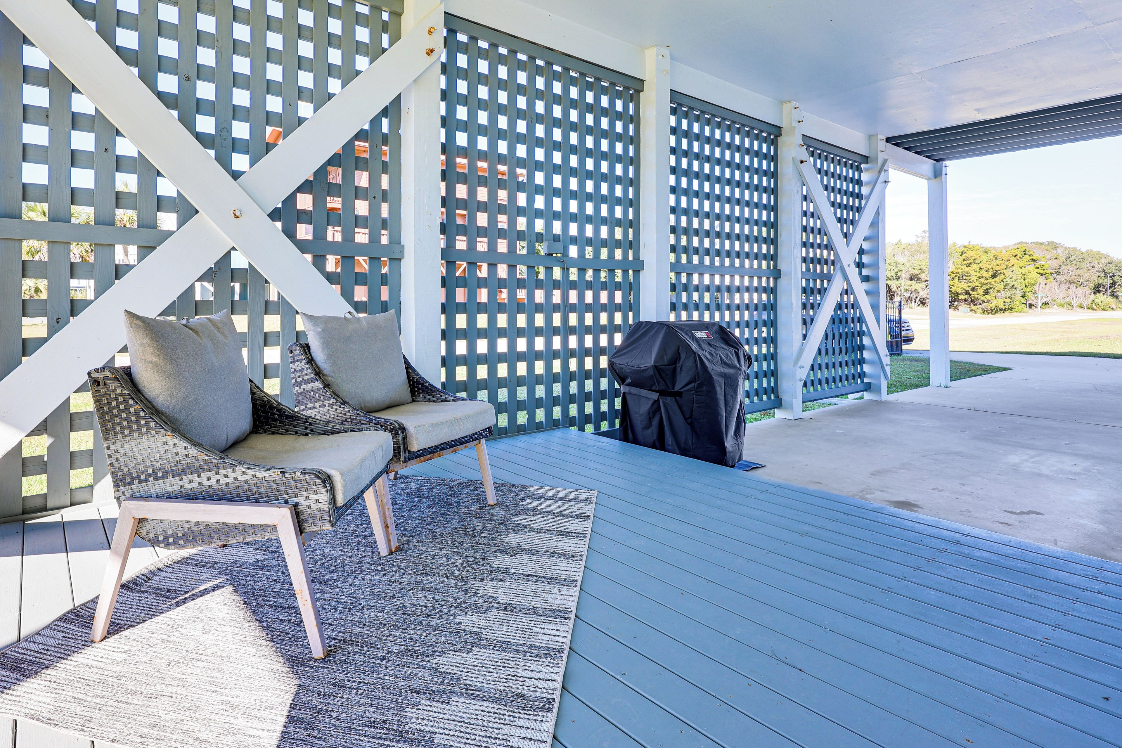 A covered outdoor seating area with a blue wooden deck, a grill, and a lattice fence.