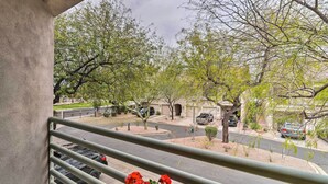 Uma varanda com vista para uma rua residencial, um carro estacionado e um edifício com fachada de pedra.