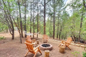 Un terrain de camping boisé, équipé de chaises en bois, d’un foyer et d’un hamac.