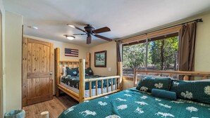 Une chambre avec un lit en bois, un ventilateur de plafond, une fenêtre avec des rideaux et une porte en bois.