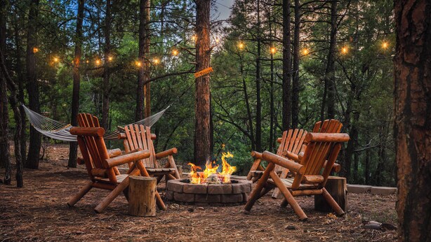 Un feu de camp avec trois chaises Adirondack et un hamac, le tout installé dans une forêt.