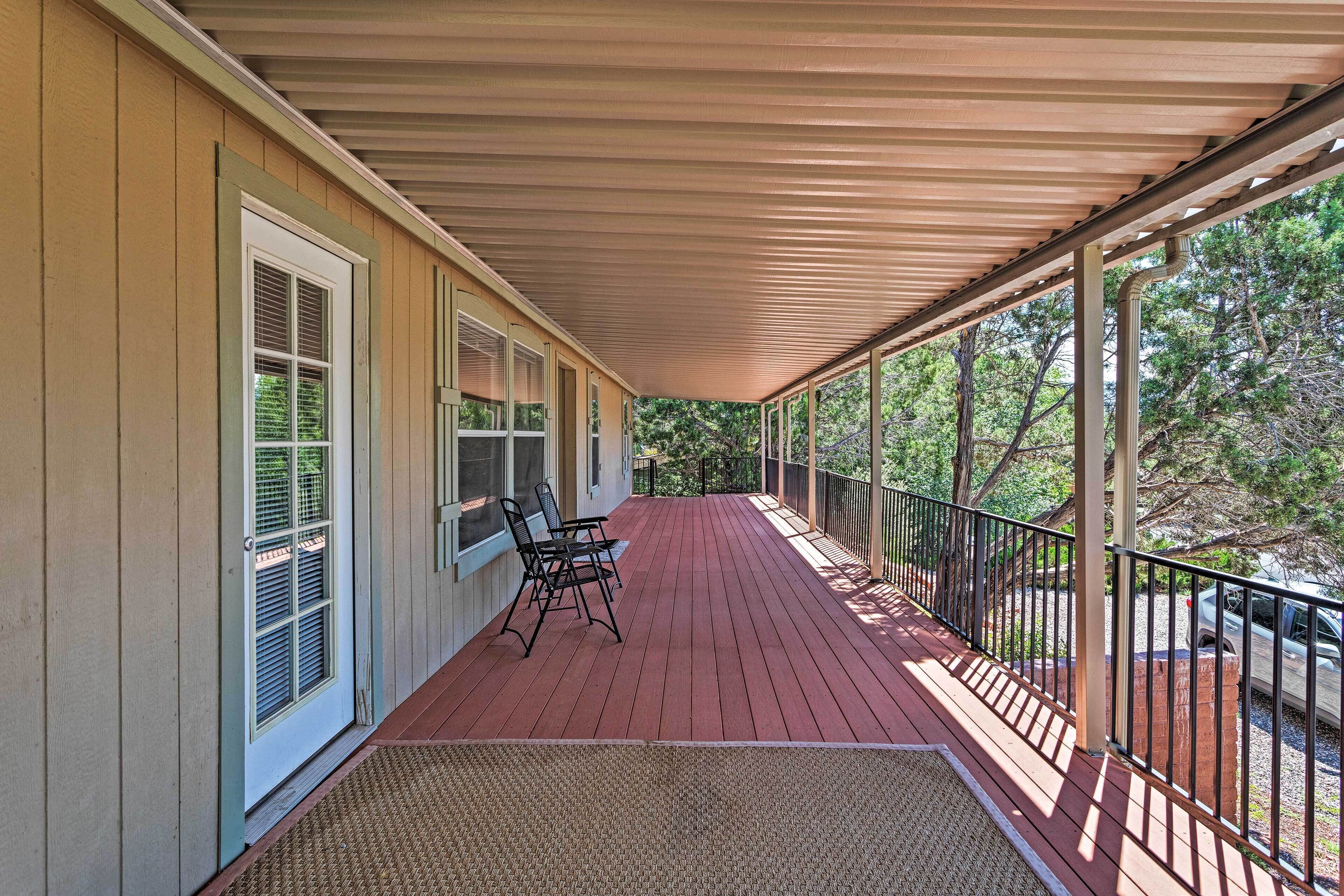 A covered porch with a red wooden floor, a black metal railing, and a bench.