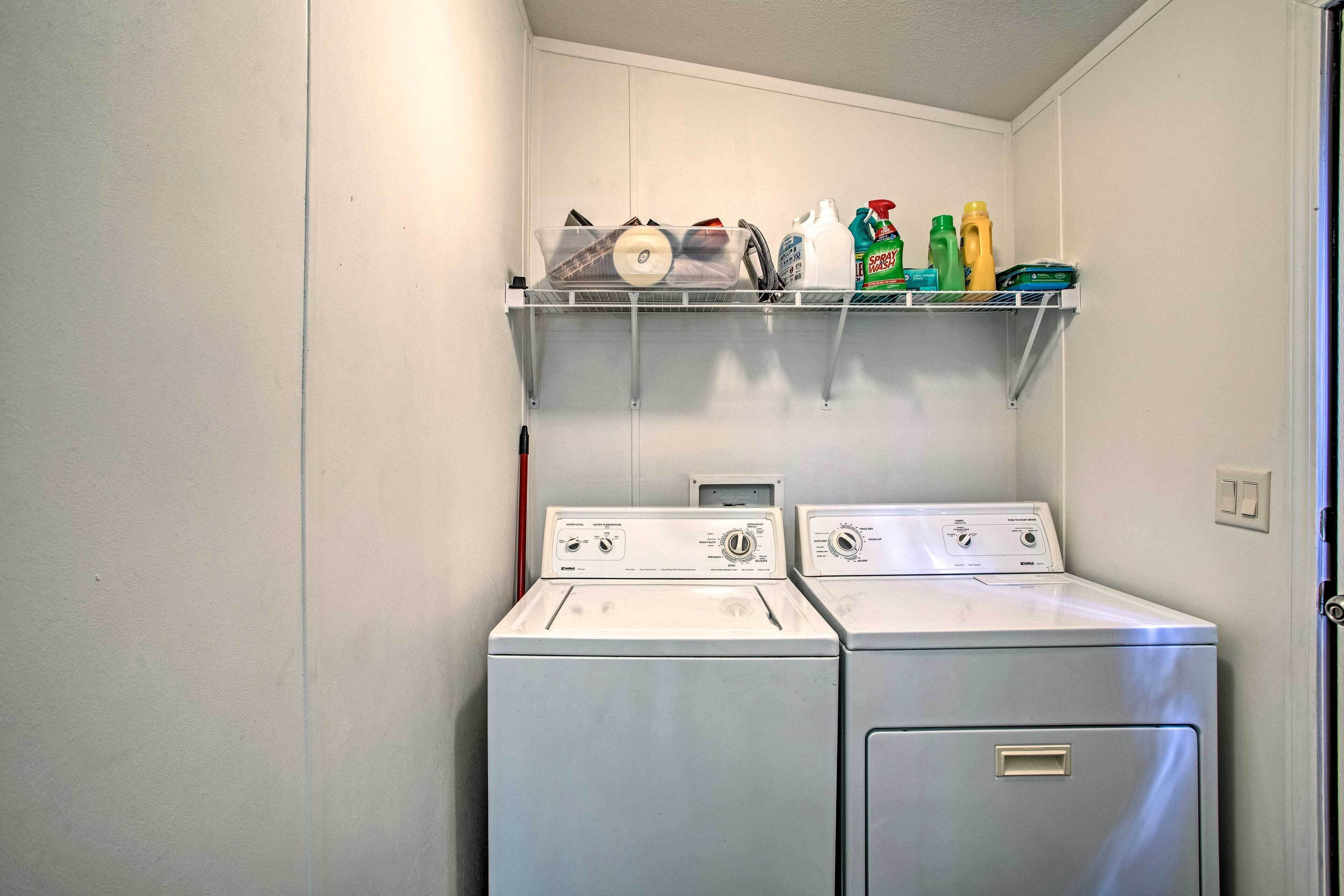 A laundry room with two front-loading washing machines and a shelf above containing cleaning supplies.