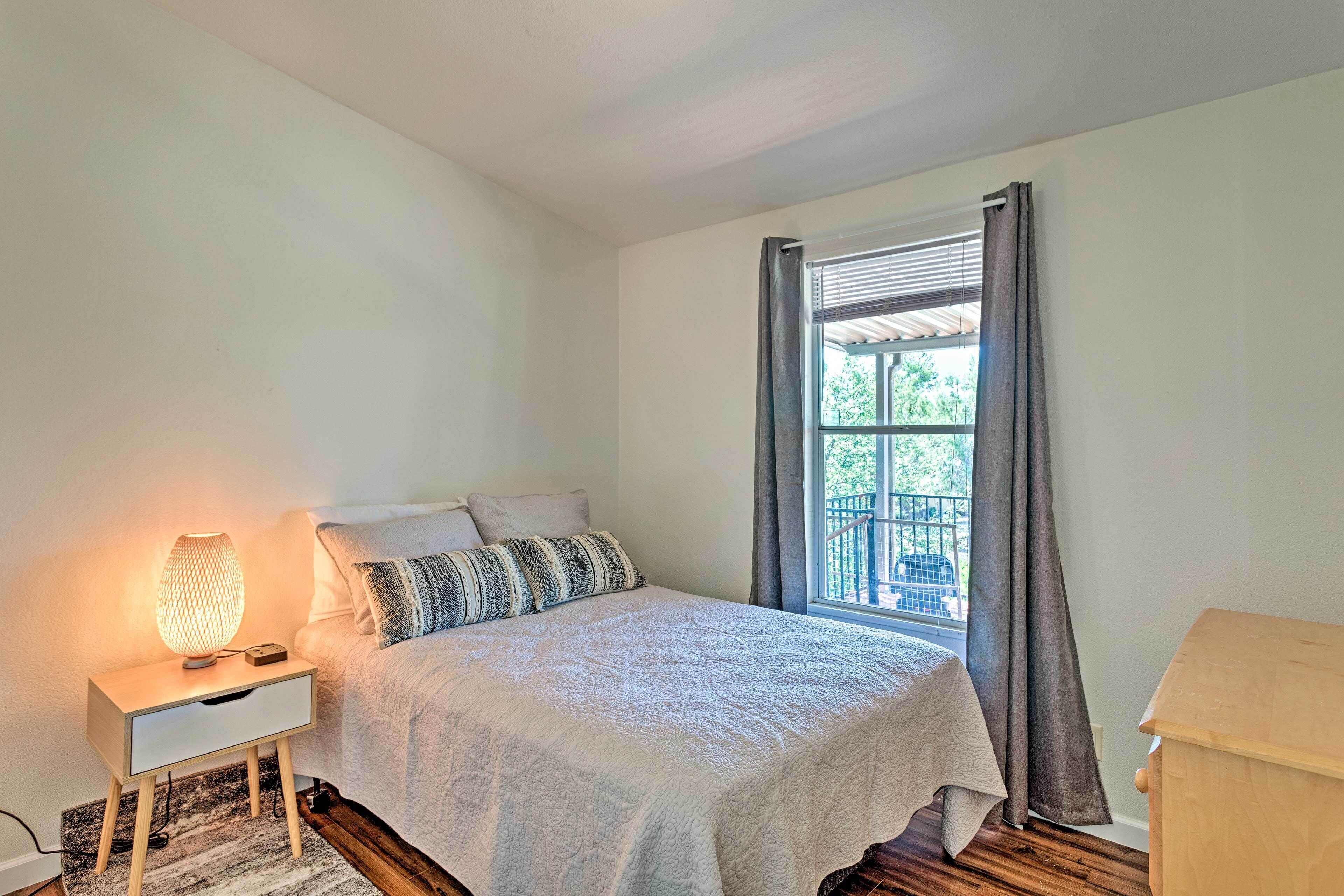 Une chambre à coucher comprenant un lit, une lampe de chevet, une table de chevet, une fenêtre avec des rideaux et une vue sur l’extérieur.