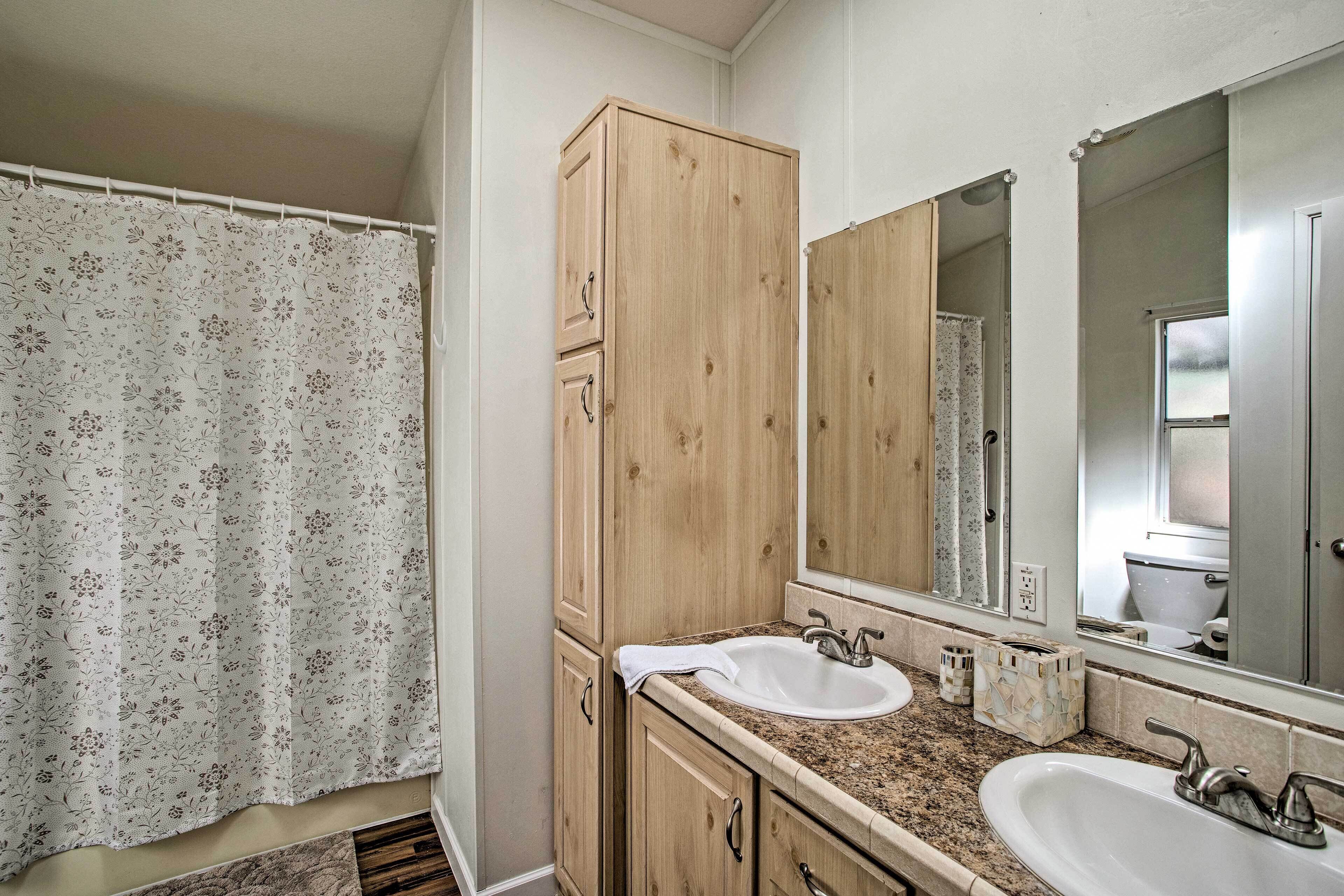 Un baño con dos lavamanos, armarios de madera, un espejo grande y una cortina de ducha.