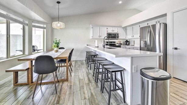 A modern kitchen with white cabinets, stainless steel appliances, a central island with bar stools, and a dining area with a wooden table and chairs. - Pool, BBQ & Patio: Gilbert Getaway Near Golfing (Gilbert)