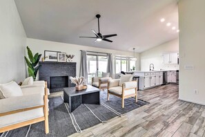 A modern living room with a fireplace, sofa, coffee table, and a view of the kitchen. - Pool, BBQ & Patio: Gilbert Getaway Near Golfing (Gilbert)