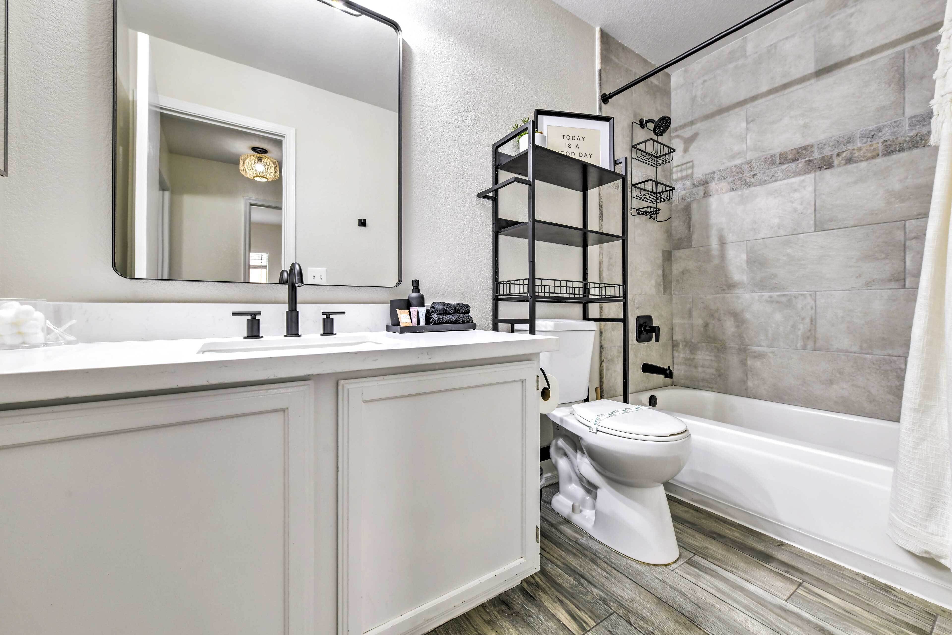 A modern bathroom with a white vanity, a large mirror, a toilet, and a shower area.