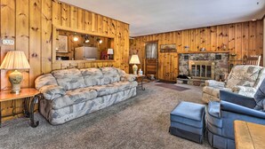 Ein gemütliches Wohnzimmer mit Holzwandverkleidung, Kamin, Sofa, Sessel und Couchtisch.