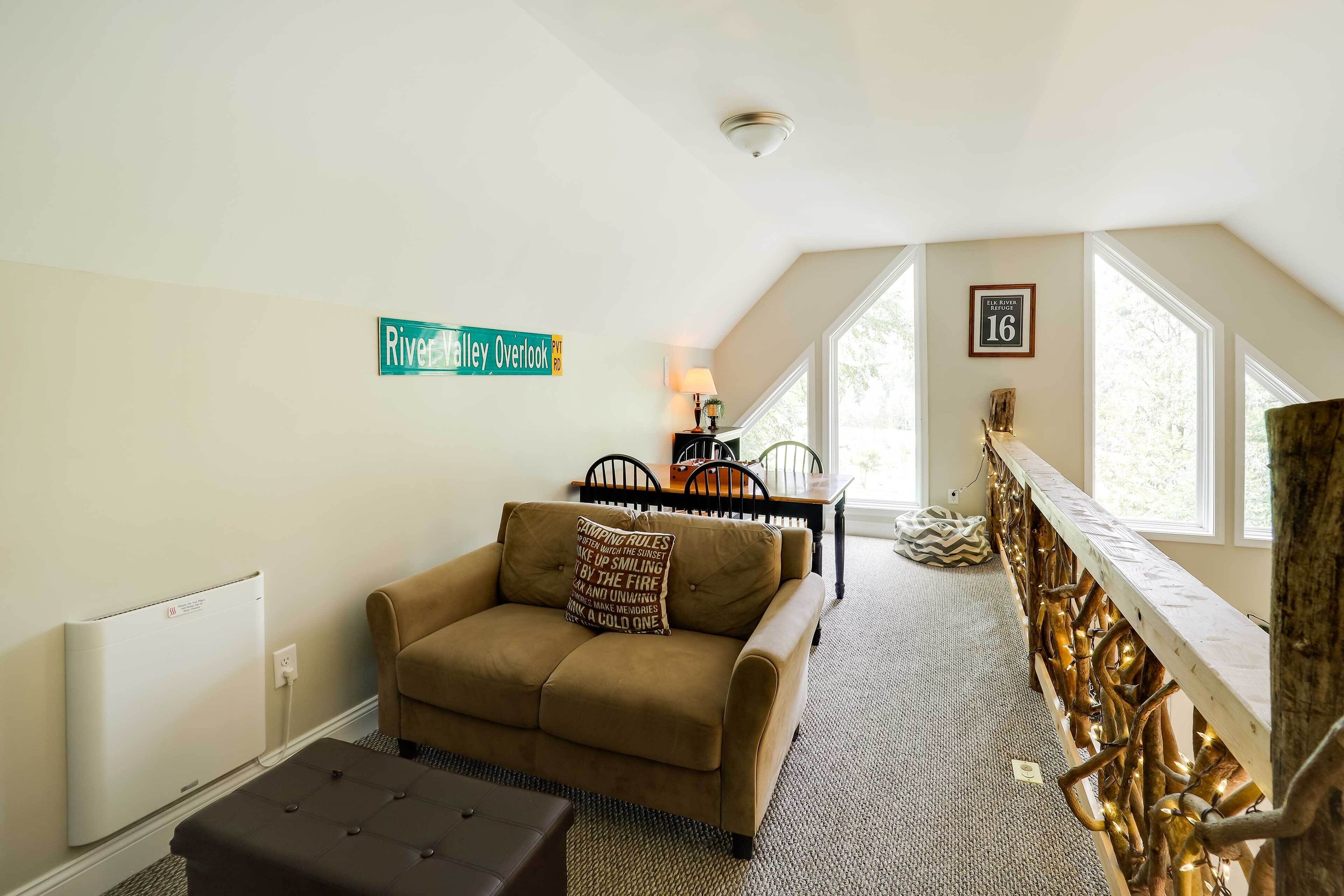A cozy room with a brown sofa, a dining table with chairs, a fireplace, and a large window.