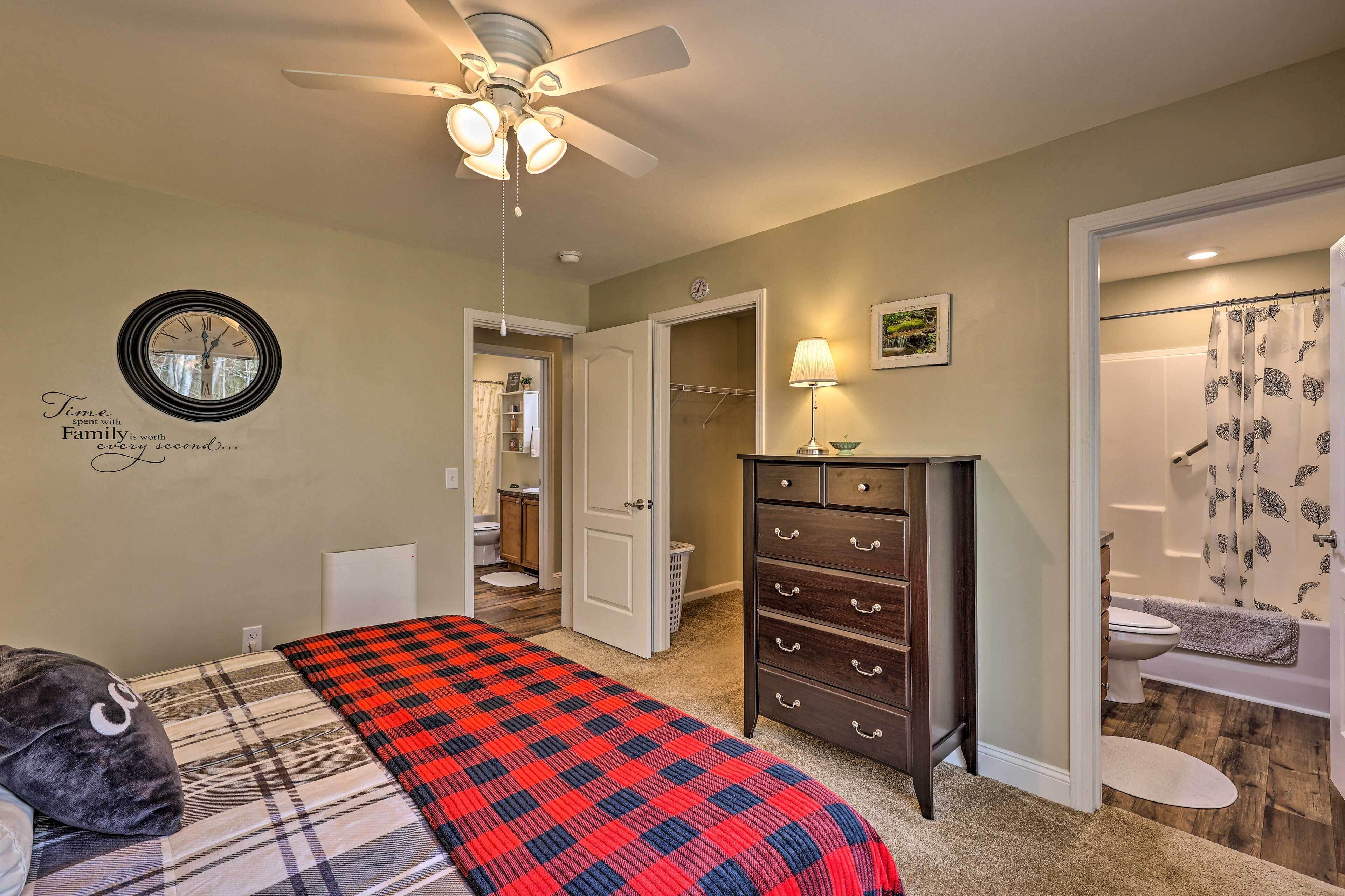 A bedroom with a bed, a dresser, a ceiling fan, a wall clock, and a bathroom visible through an open door.