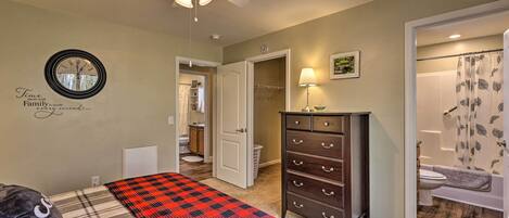 A bedroom with a bed, a dresser, a ceiling fan, a wall clock, and a bathroom visible through an open door.