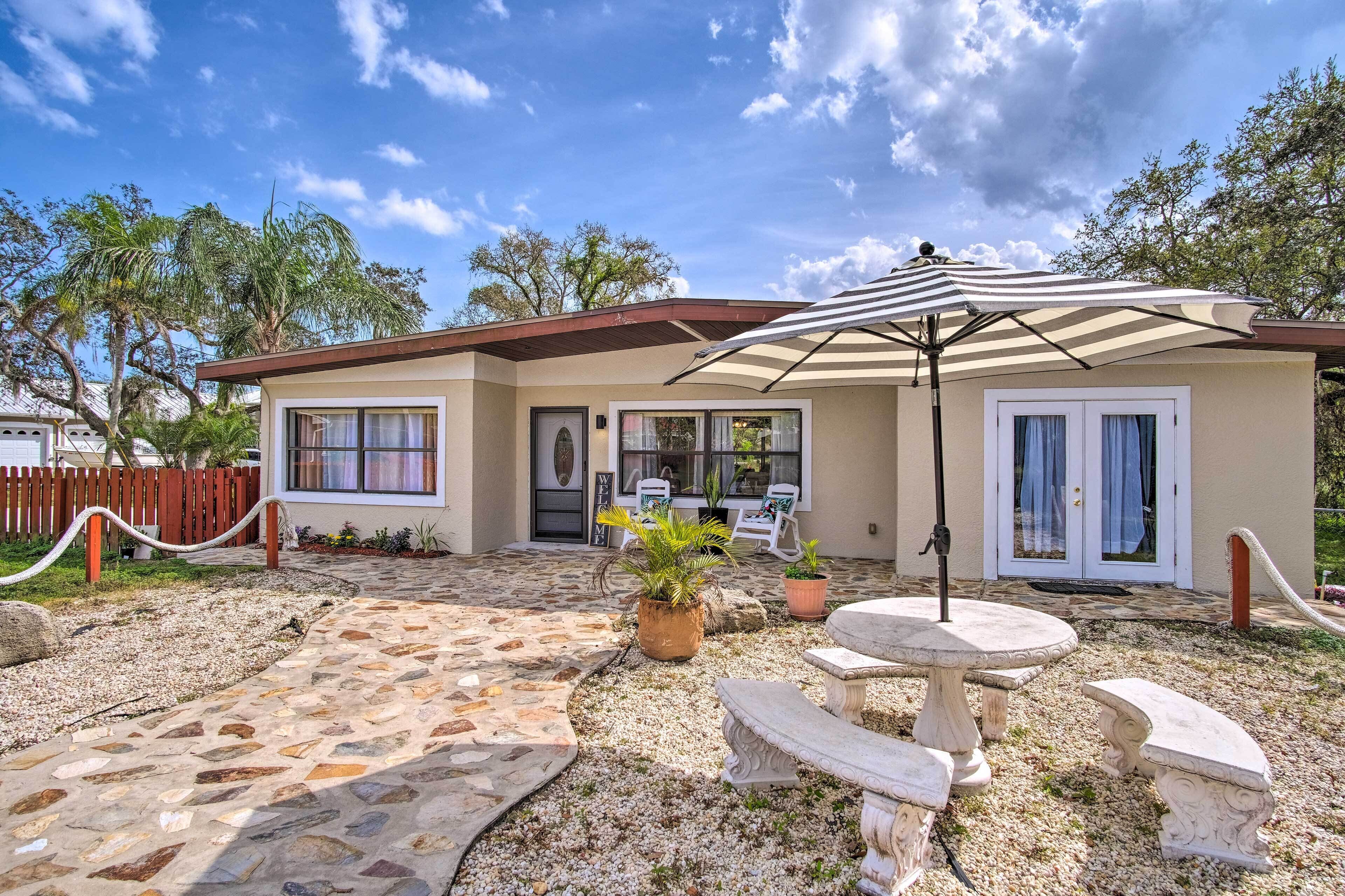 A house with a patio area featuring a stone pathway, a table with an umbrella, and potted plants.