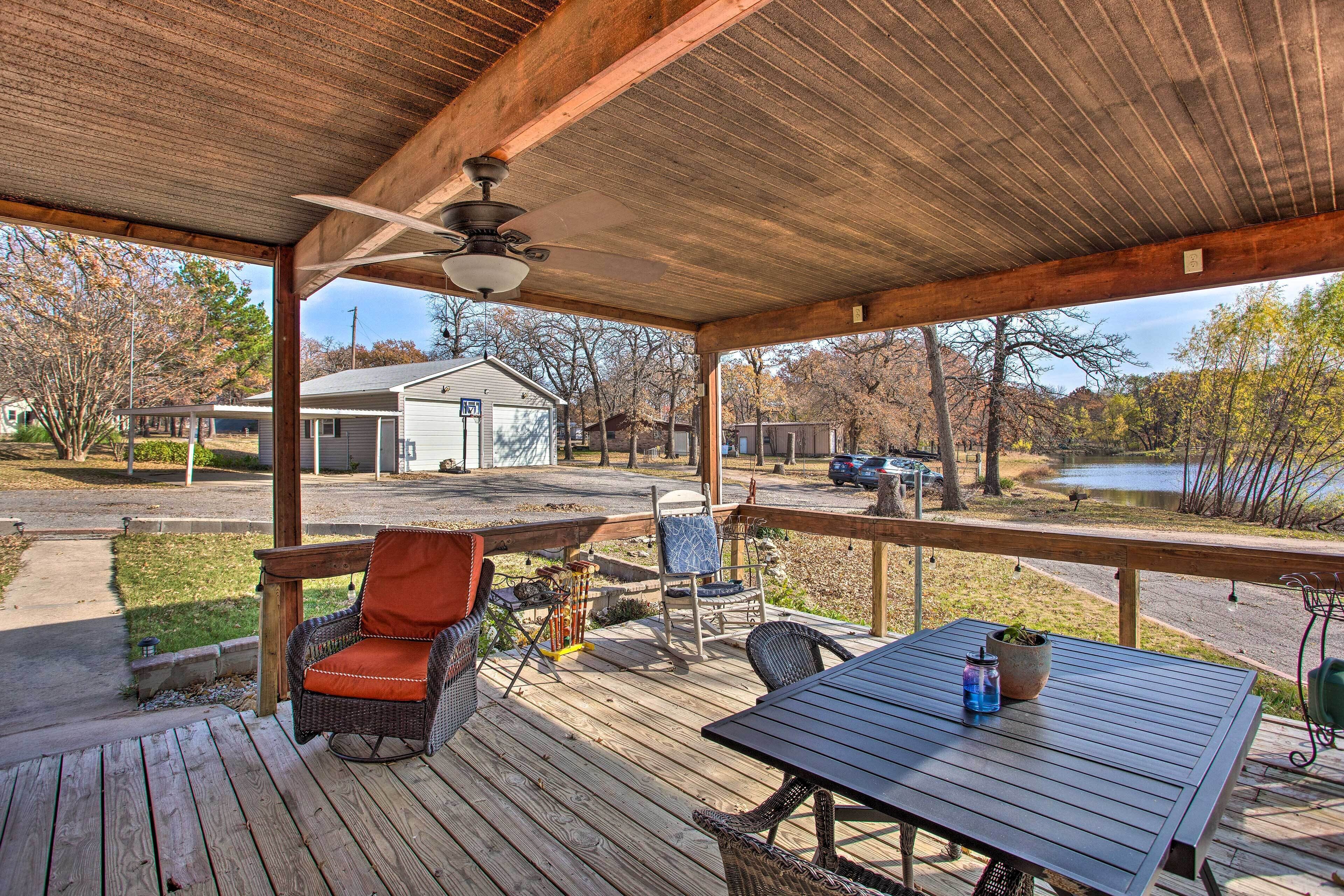 A covered deck with a table and chairs, overlooking a residential area and a body of water.