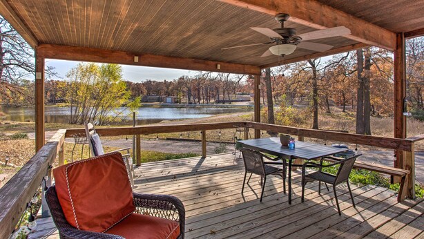 Una terraza de madera con una mesa y sillas, con vista a un lago y árboles.