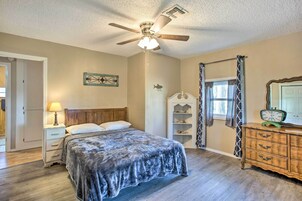 A bedroom with a bed, a nightstand, a dresser, a ceiling fan, and a window with curtains.