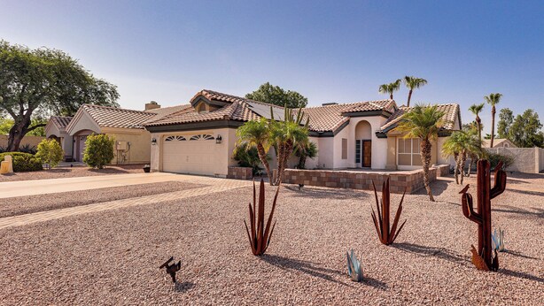 Un quartier résidentiel où se trouve une maison avec un toit en tuiles, une allée gravillonnée et plusieurs cactus.
