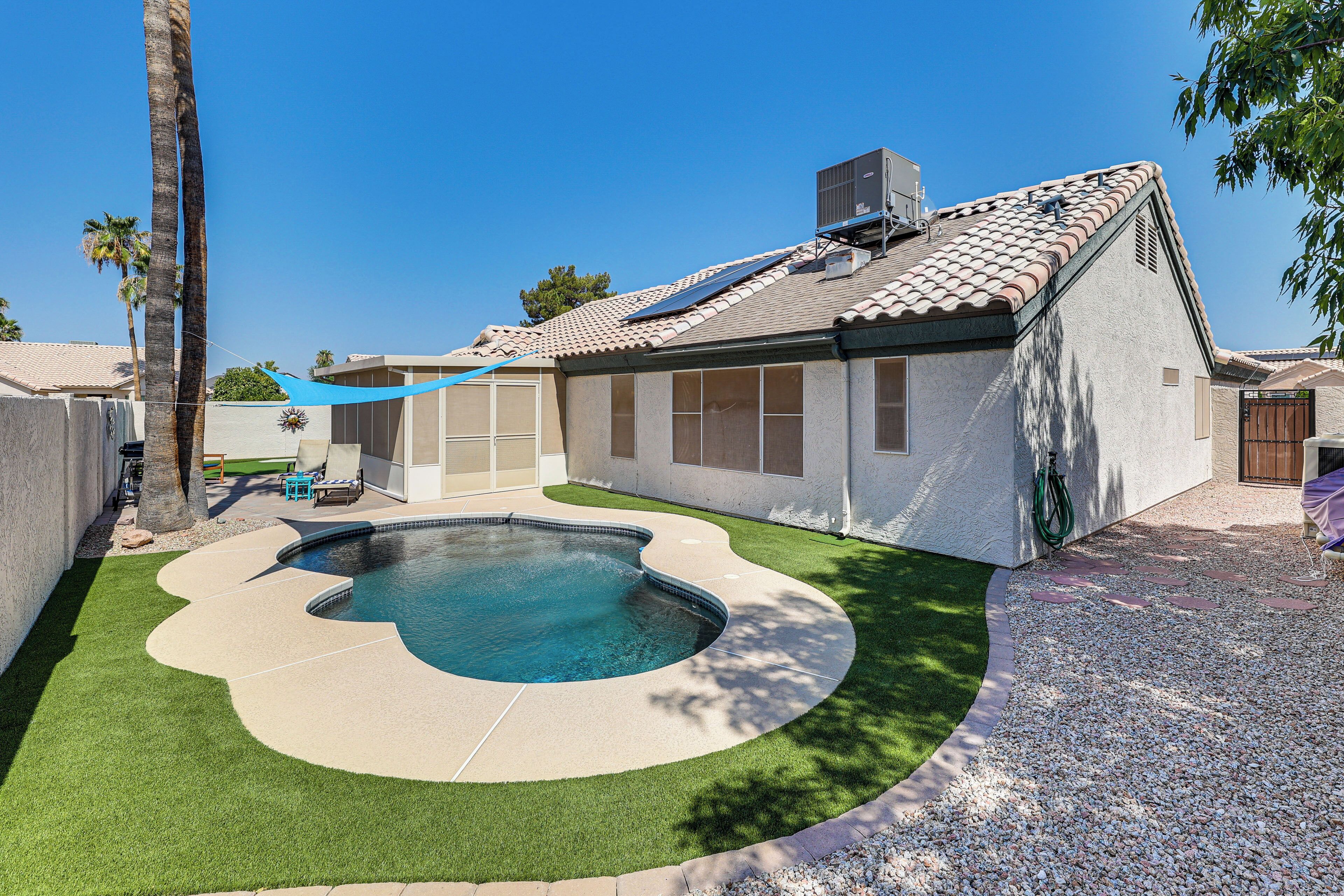 Un jardin à l’arrière d’une maison, avec une piscine, des panneaux solaires et un patio couvert.