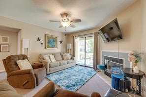 Ein Wohnzimmer mit einem braunen Liegesessel, einem beige farbenen Sofa, einem flauschigen, blauen Teppich, einem Flachbildfernseher und einem Kamin.