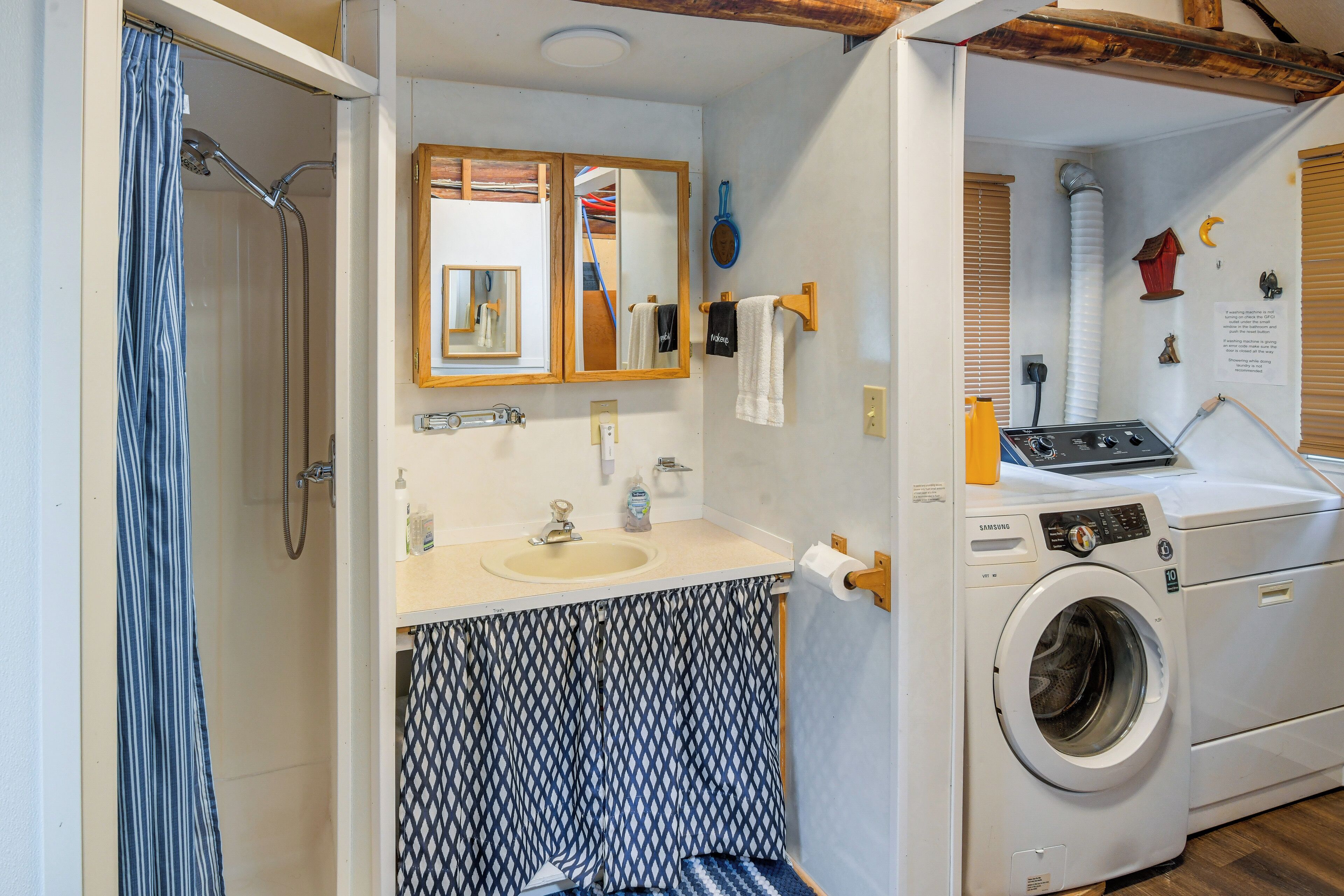 A compact bathroom with a shower, sink, mirror, and a front-loading washing machine.