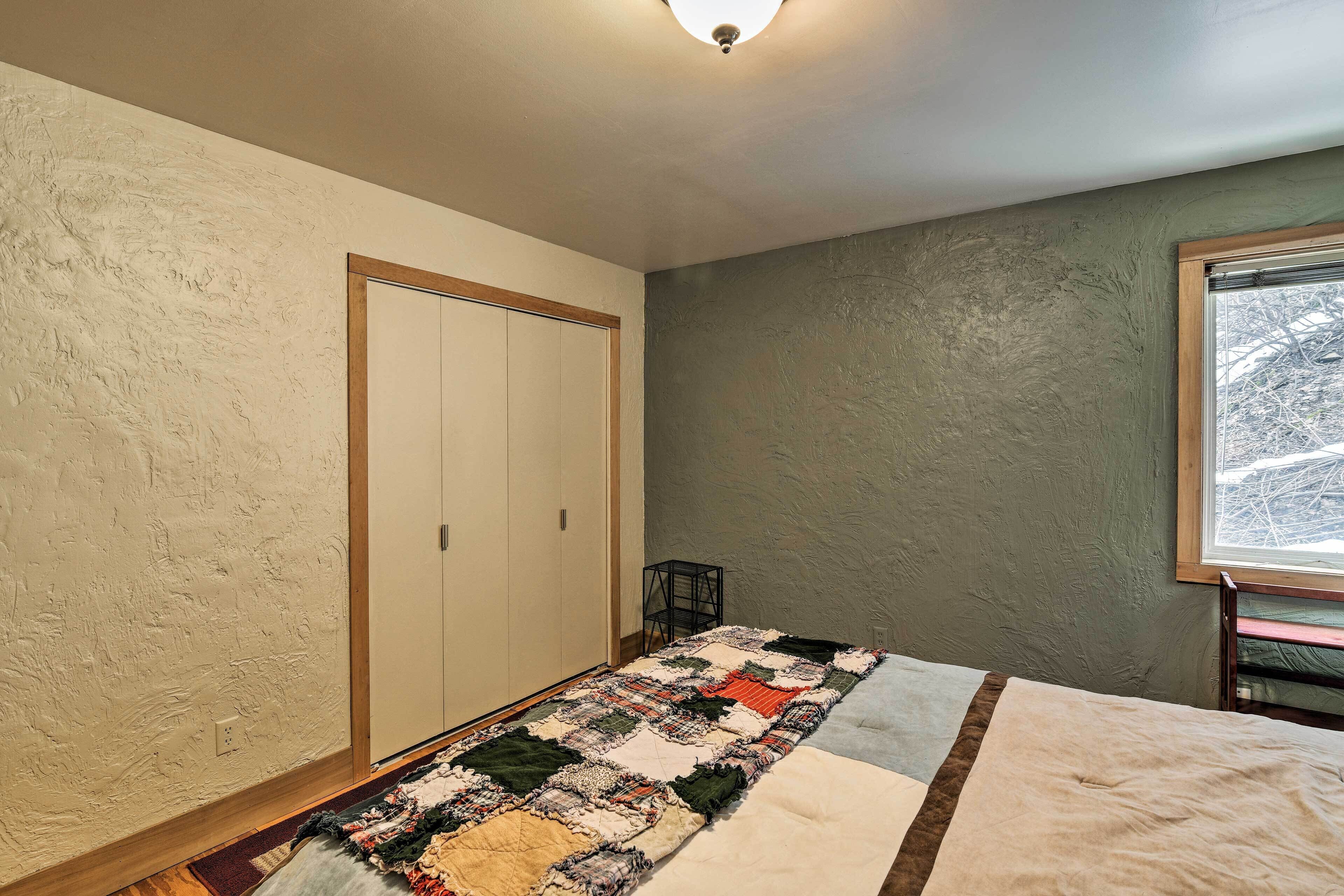 A bedroom with a bed, a quilt, a wardrobe, and a window with a view of trees.