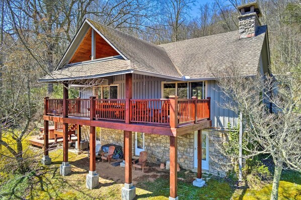 A two-story cabin with a wooden deck and stone foundation, surrounded by trees. - 40-acre Mtn-view Retreat w/ Hot Tub in Banner Elk! (Banner Elk)