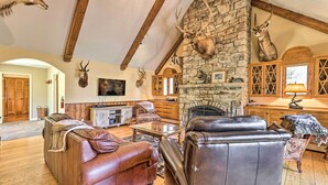 A spacious living room with leather sofas, a stone fireplace, and mounted animal heads.
