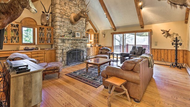 A cozy living room with a stone fireplace, wooden furniture, and mounted animal heads.