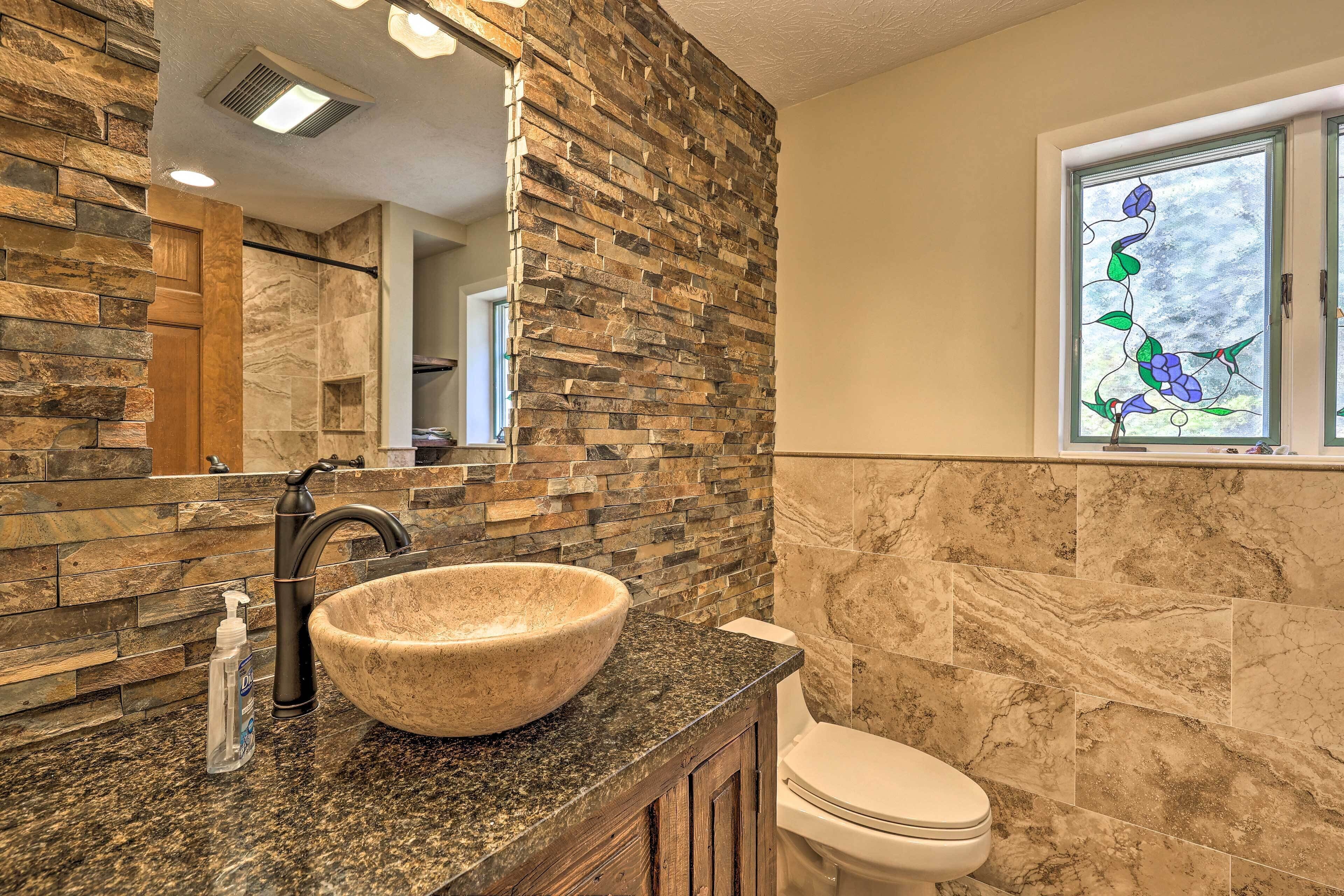 A bathroom with a stone wall, a large sink, and a window with a floral design.