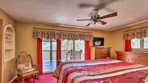 A bedroom with a large bed, a wooden chair, a dresser, a television, and a balcony with red curtains.