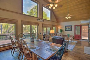 A dining area with a wooden table set for four, surrounded by wooden chairs, a red door, and a view of trees through large windows. - Lake Granbury Getaway! Family Home w/ Deck & Games (Granbury)