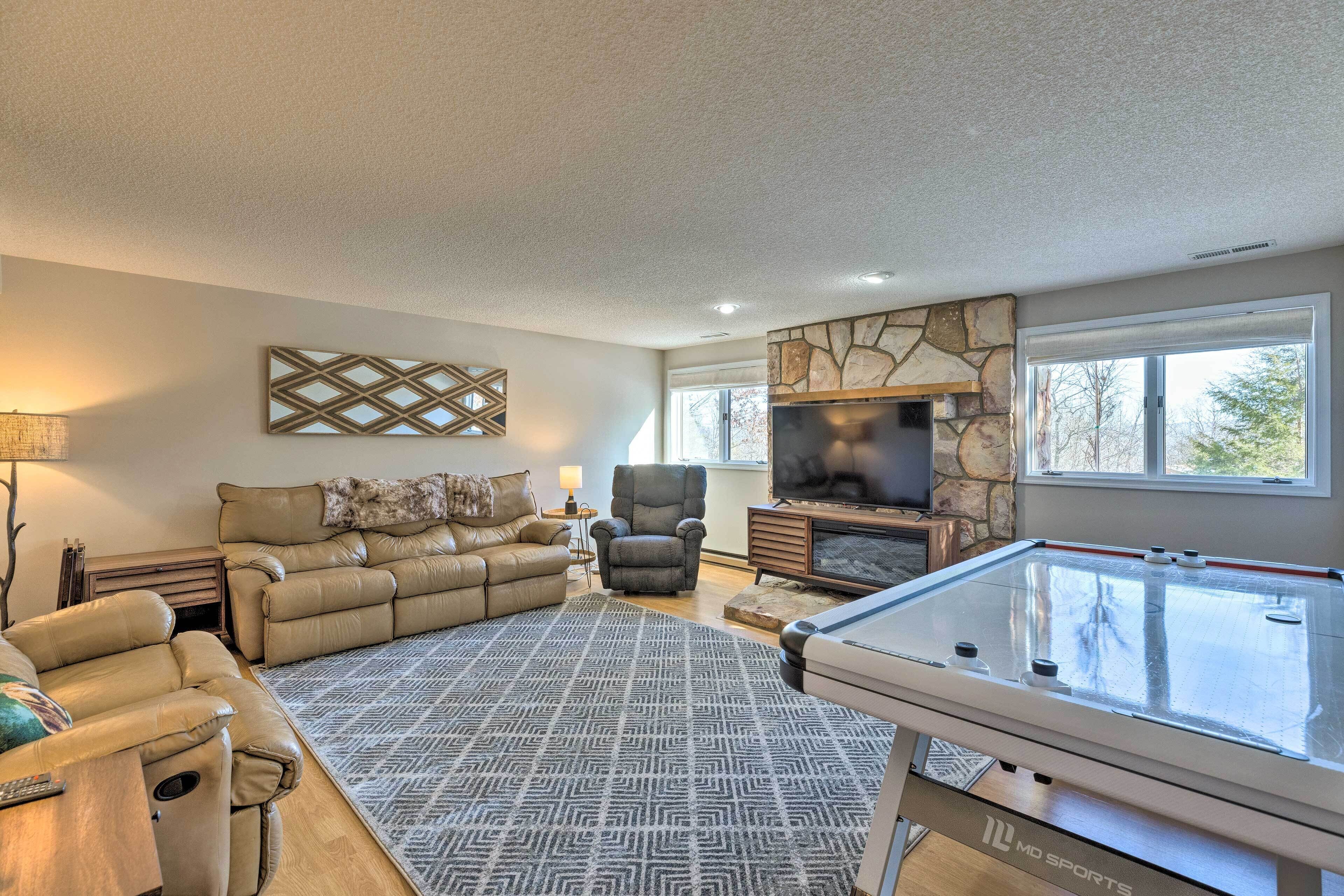 A living room with a pool table, leather sofas, a stone fireplace, and a TV.