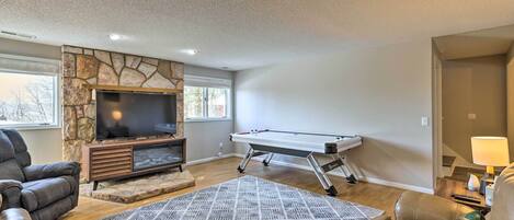 A living room with a stone fireplace, a flat-screen TV, a pool table, and leather sofas.