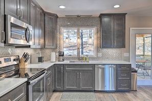A modern kitchen with dark cabinets, stainless steel appliances, and a large window overlooking a snowy landscape. - Massanutten Resort Home w/ Deck + Mountain Views! (McGaheysville)