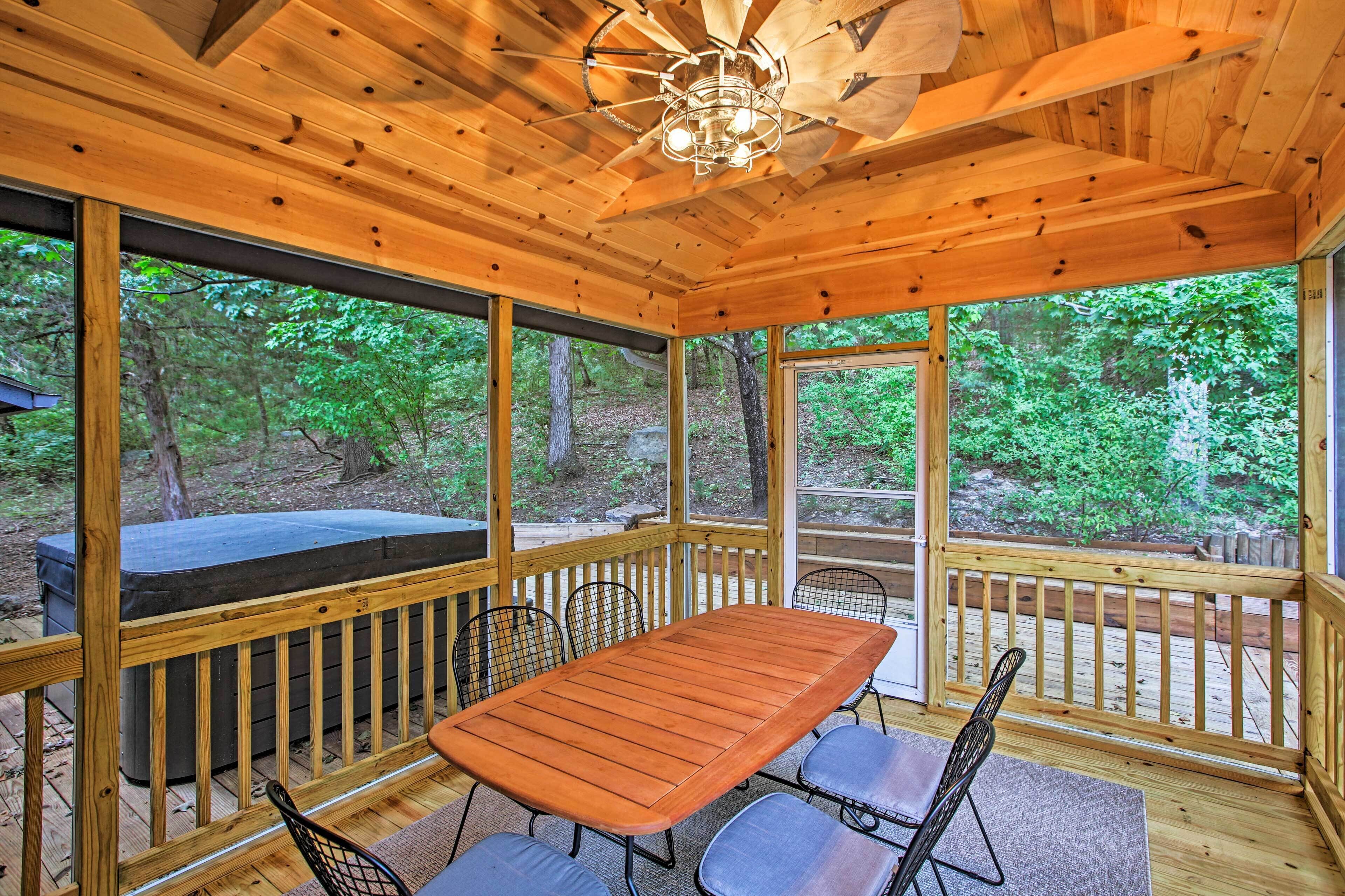A wooden deck with a table and chairs, surrounded by large windows offering a view of the forest.