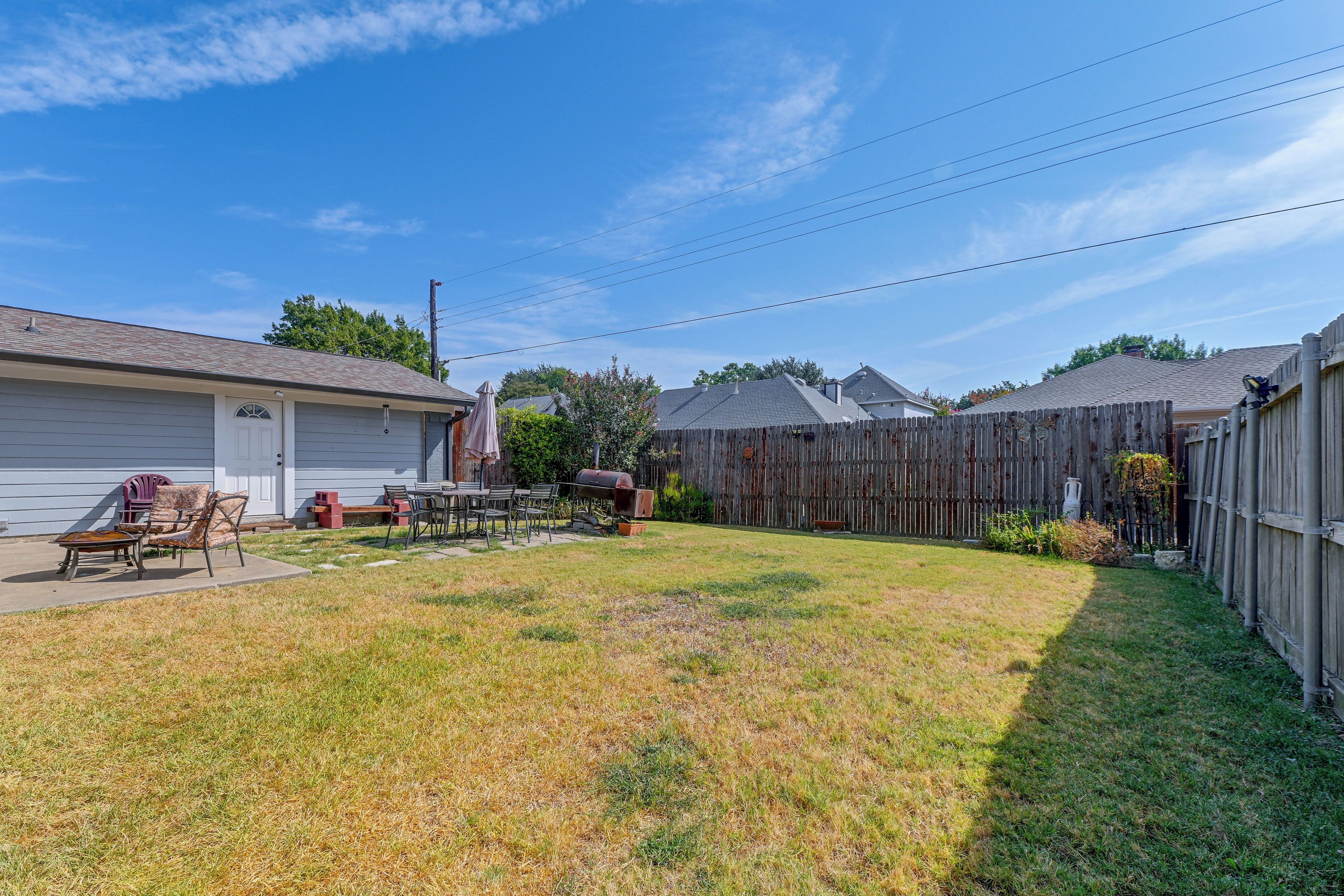 A residential backyard with a barbecue area, outdoor furniture, and a wooden fence.
