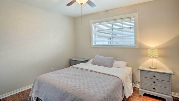 A bedroom with a bed, a nightstand, a lamp, a ceiling fan, and a window with blinds. - Stay Near All Family Entertainment in Dallas (Richardson)