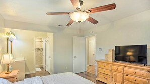 Une chambre à coucher comprenant un lit, une commode en bois, un téléviseur et un ventilateur de plafond.