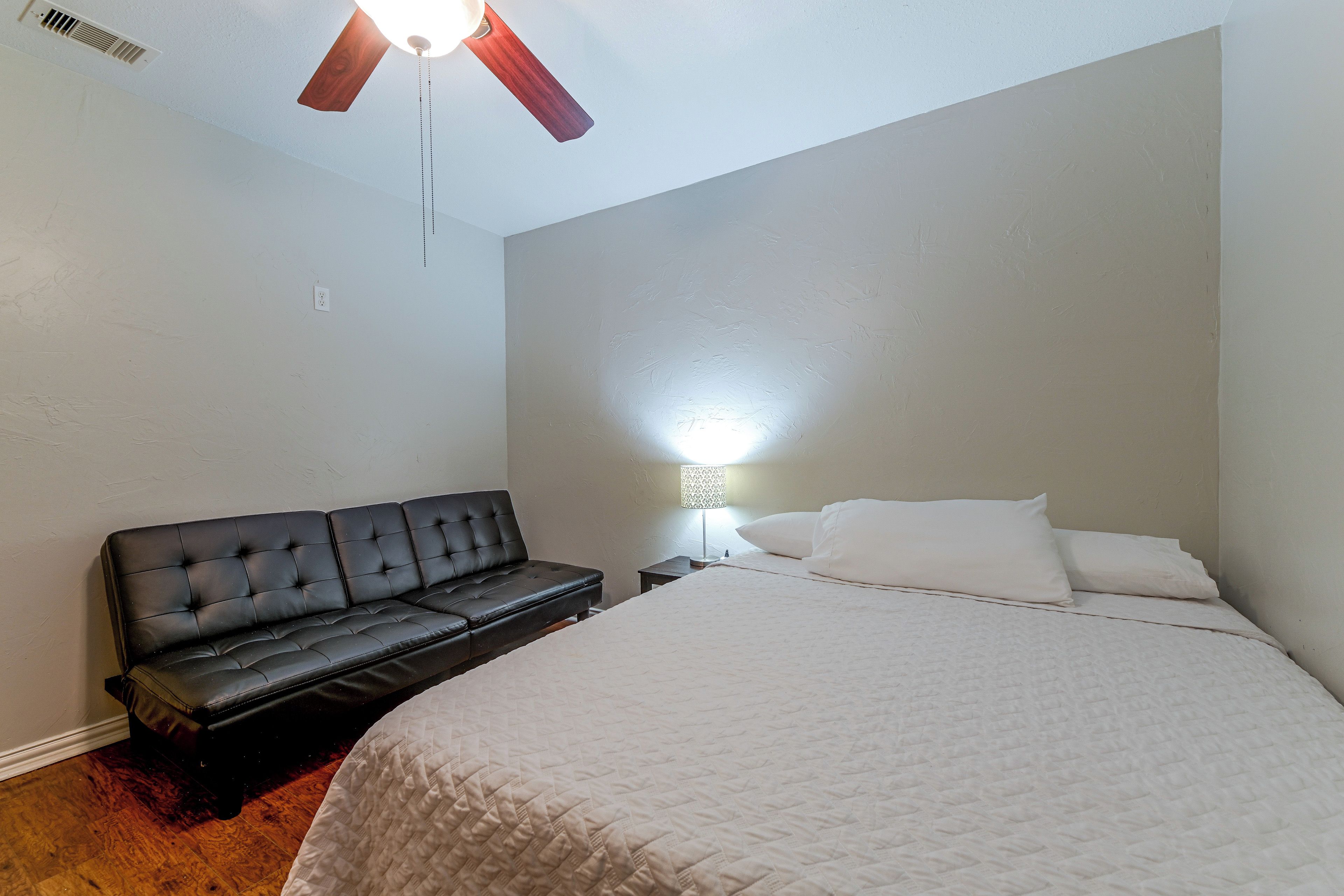Une chambre à coucher avec un lit, un canapé en cuir noir, un ventilateur de plafond et une lampe de chevet.