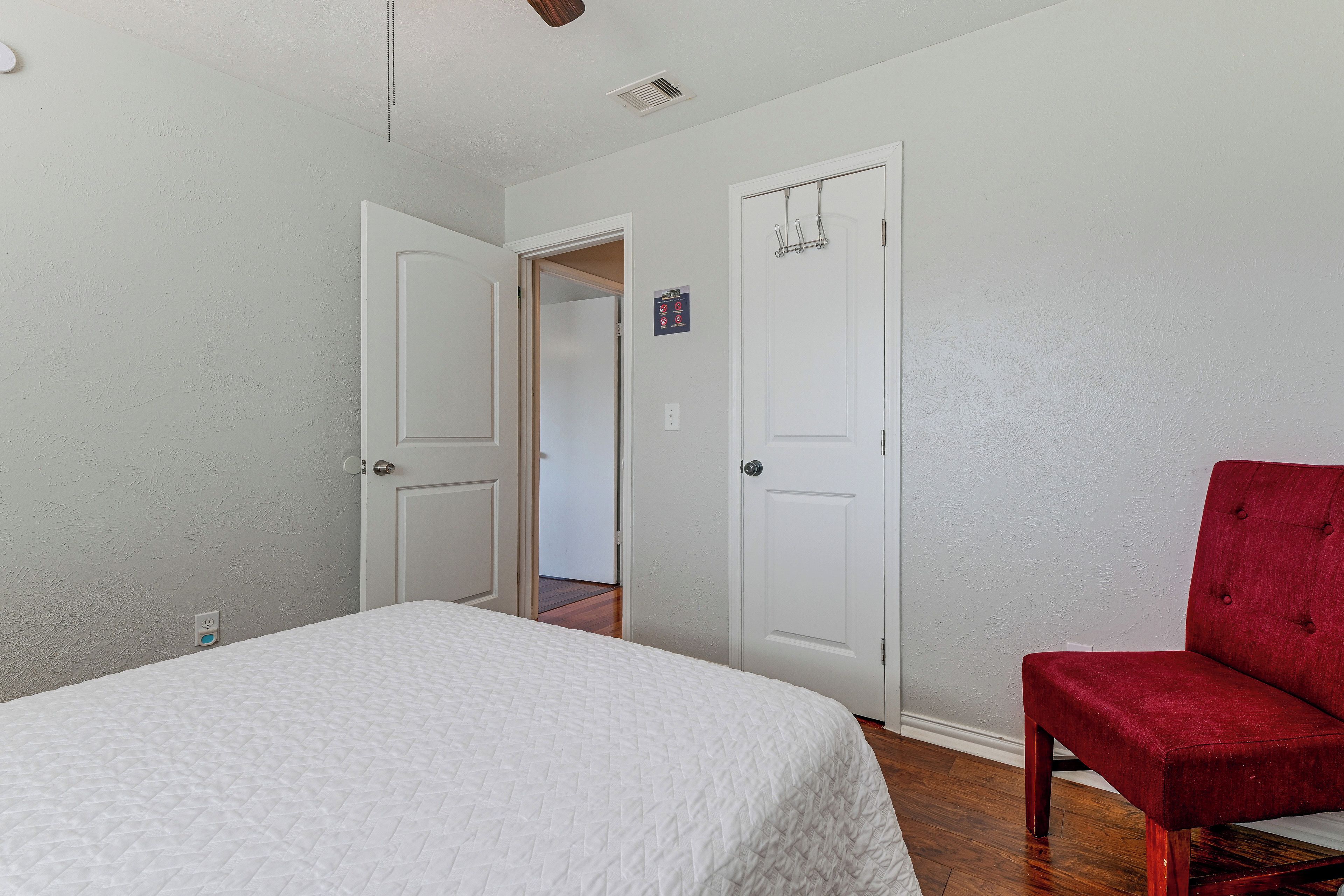Un dormitorio con una cama, una silla roja y dos puertas blancas que dan a otras habitaciones.