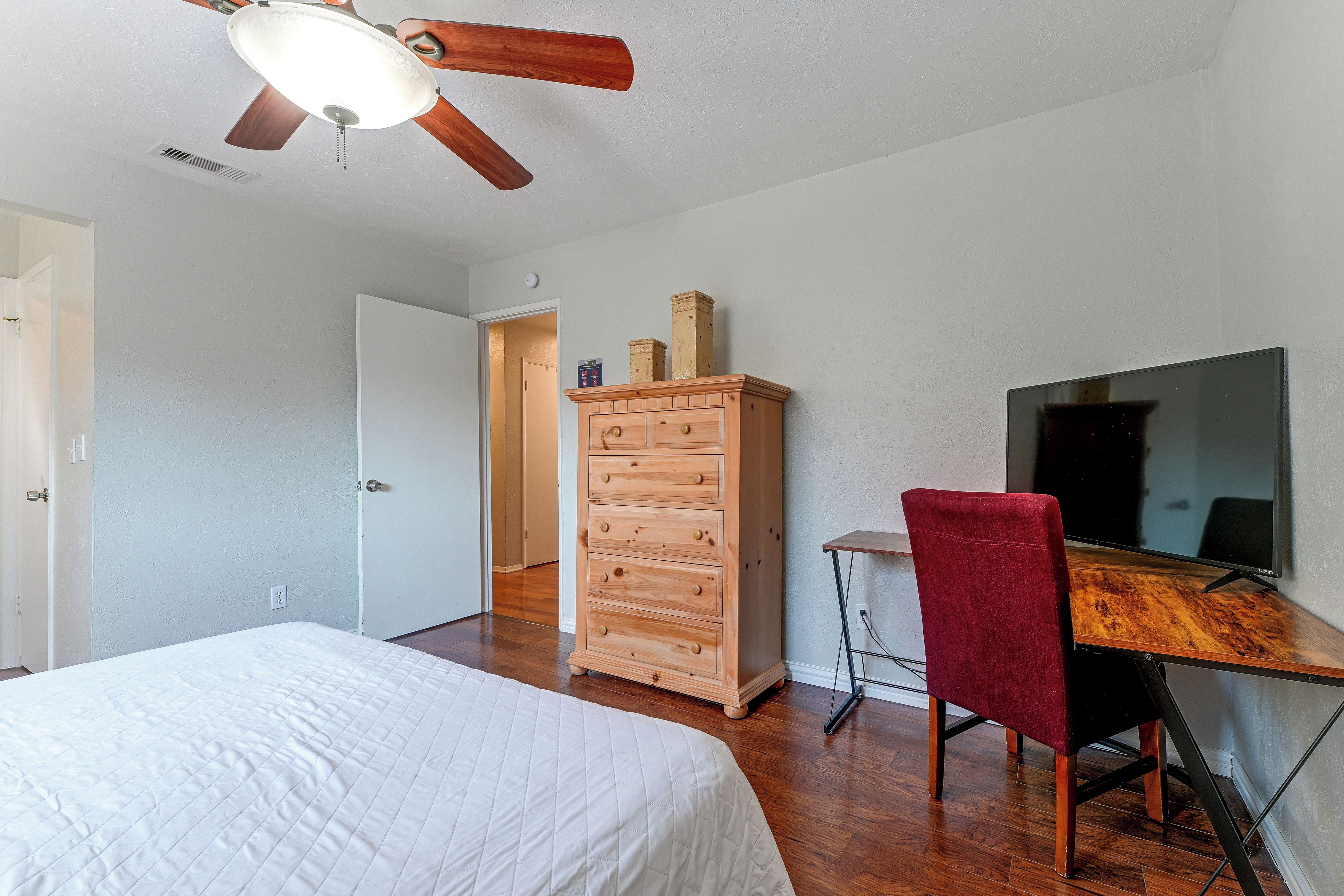 Ein Schlafzimmer mit einem Bett, einer Holzkommode, einem Schreibtisch mit Stuhl, einem Deckenventilator und einem Fernseher.