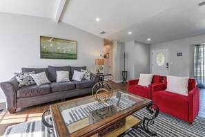 A living room with a grey sofa, a red sofa, and a glass coffee table. - Stay Near All Family Entertainment in Dallas (Richardson)