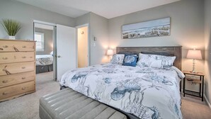 A bedroom with a bed, a dresser, a bench, a painting, and two lamps.